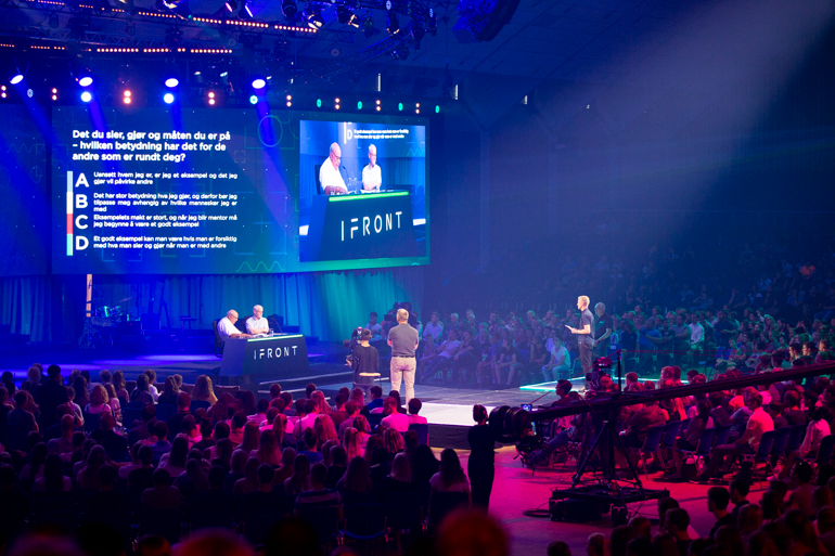 ><br><em>Alt er klart for konkurranse i storsalen, hvor hele publikum blir involvert til å delta via mobiltelefonene sine. Foto: BCC</em></p>
<p>Salen er inndelt i to soner som konkurrerer mot hverandre, og publikum utfordres til å svare på spørsmål via mobiltelefonene.</p>
<p>Eldre voksne som har jobbet som ungdomsarbeidere hele sitt voksne liv vil delta aktivt med veiledning og gode innspill fra scenen, og forstander Kåre Smith er av de som skal utdype temaene ytterligere underveis. På en spennende måte gir konkurransen ny innsikt om trosrelaterte, hverdagslige spørsmål som de unge kunne kjenne seg igjen i.</p>
<p>Laglederne Harald Kronstad og Trond Eriksen har gjort seg klare, og forberedt korte innlegg til hvert tema som det konkurreres i. De håper programmet kan oppmuntre og lære ungdommene noe viktig, samtidig som mens de klikker på ulike svaralternativer på mobiltelefonene og hører juryens begrunnelse for det beste svaret.</p>
<p><img decoding=