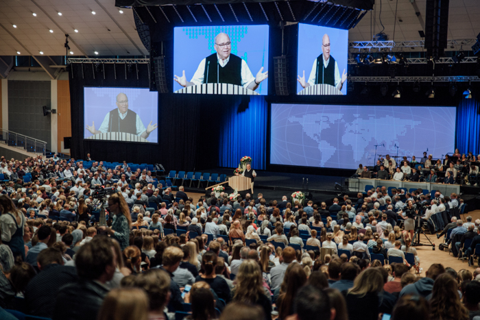 ><br><em>Den store salen på Oslofjord Convention Center rommer flere tusen tilhørere </em></p>
<p><strong>Utvikling i fasiliteter og teknikk</strong></p>
<p>Pinsestevnene går mange år tilbake, og det første pinsestevnet vi kjenner til ble avholdt i Drøbak i 1913. Noen år senere, i april 1925, kunne man lese følgende i menighetens blad Skjulte Skatter; «<em>Pinsestevne avholdes om Gud vil paa Horten. Brødrene bør ta med teppe og hodepute og overnatte paa lokalet. Alle tar med niste. Kaffe og melk faaes på lokalet. Fjerntliggende trakter bør sende utsendinger</em>». Tidene skifter, og selv om det er fint med utsendinger, er det positivt at flere i dag har mulighet til å reise og være tilstede på BCCs stevner. Konferansene avholdes i dag i topp moderne konferansefasiliteter. Denne helgen sørget over 50 medarbeidere i BrunstadTV-crewet for at lys-, lyd- og bildeteknikk var på plass i salen, i tillegg til at hele konferansen ble direktesendt til medlemmer over hele verden, via satellitt-TV og nettstreaming.</p>
<p><img decoding=
